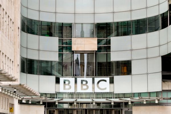 The BBC logo on Broadcasting House, a large, curved, glass-fronted building.