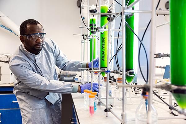 A researcher in a lab coat working with test tubes and machinery in a lab