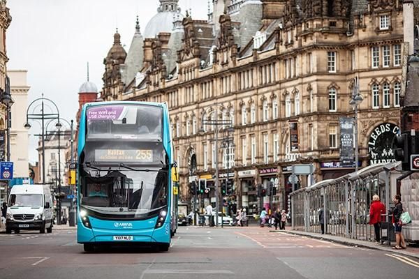 Bright blue bus driving down Leeds city centre street with old buildings on either side