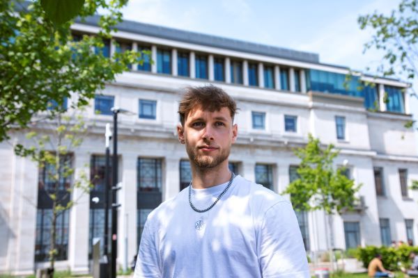 A student stands looking ahead, with the face of the Sir William Henry Bragg building in the background.
