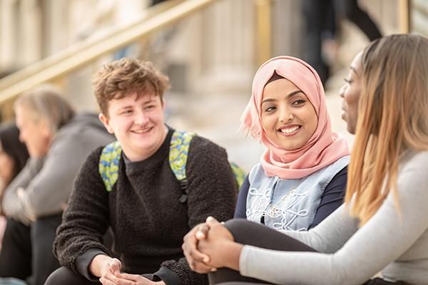 Three students having a conversation sitting on the Parkinson Building steps.