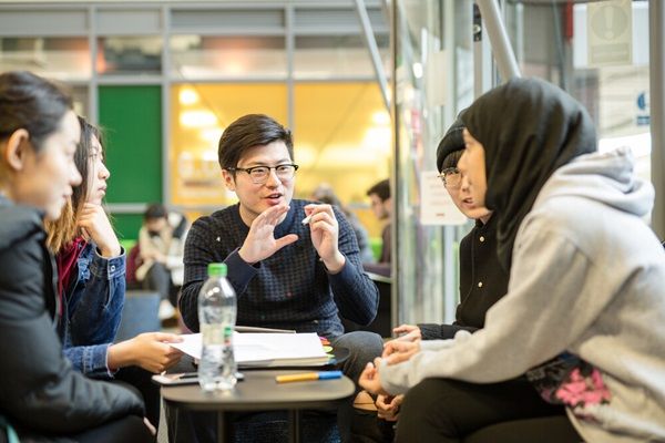 A group of students sat around a table chatting in a communal space on campus