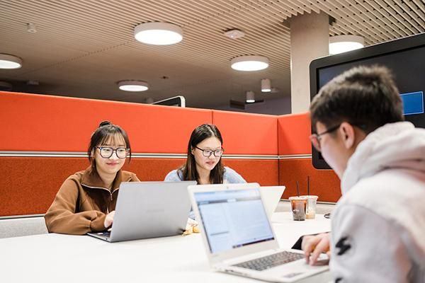 Three students sitting around a desk, looking at laptops