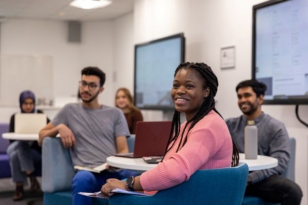 A group of students sit around tables in a classroom, looking forwards and smiling