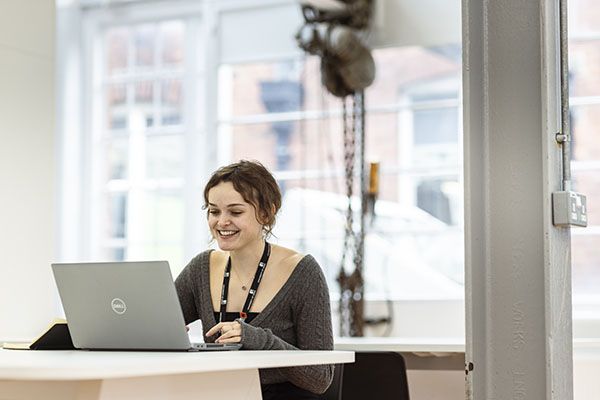 A student working on a laptop by a bright window.