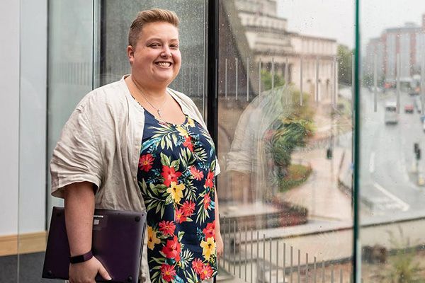 Carole stood smiling with a laptop in the large glass windows of the Laidlaw Library, overlooking Woodhouse Lane.