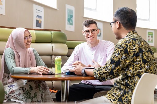 Three students sat at a table in a bright communal space on campus.