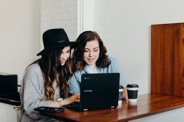 Two people looking at a laptop on a desk, with coffee cups next to it.