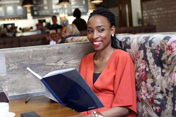 Student sat in cafe smiling with a book.