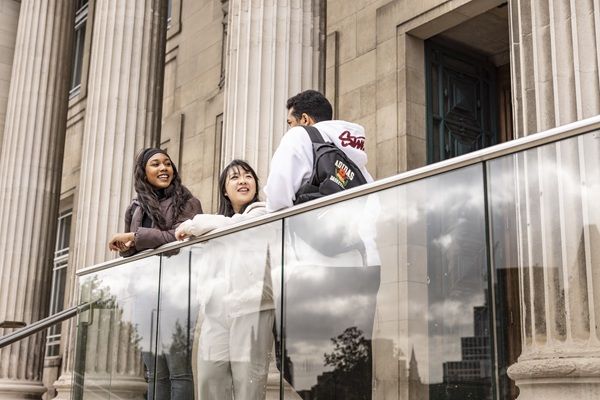 Three students stood in front of the Parkinson Building entrance chatting and smiling.