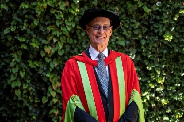 Ed Anderson stands smiling at the camera in red and green robes and a black cap.
