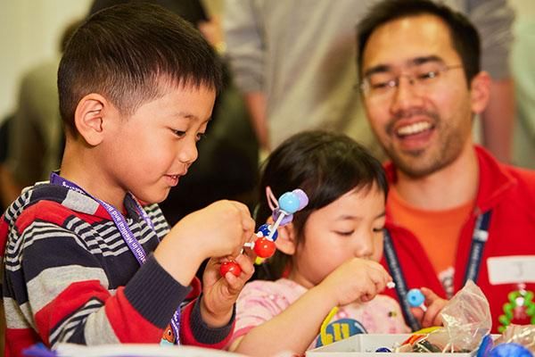 A family with two children building models at a Be Curious event.