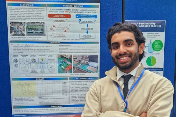 Farhan stands, smiling at the camera, in front of a blue board on which are pinned his research documentation