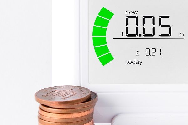 A smart energy meter, showing numbers, with a stack of coins in front of it