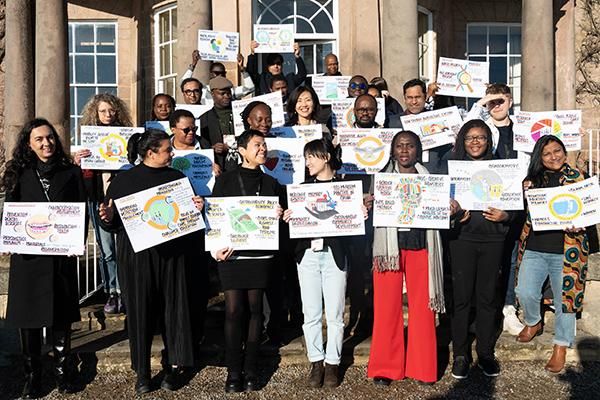 Participants from the Global Crucible 2024/25 cohort pose in a group with posters showing graphic depictions of their research