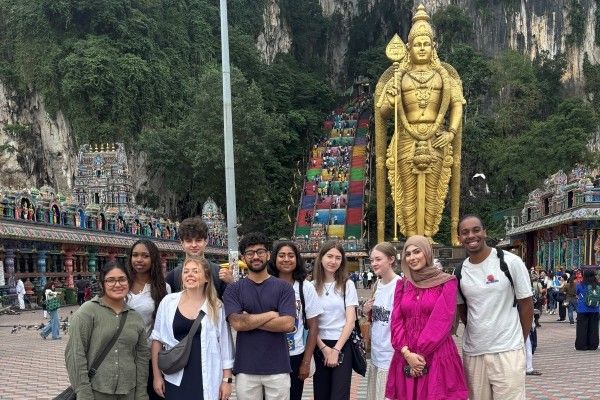 A group of ten students stand in front of tall gold statute and Batu Caves.