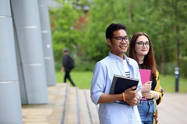 Two students standing together outside holding books.