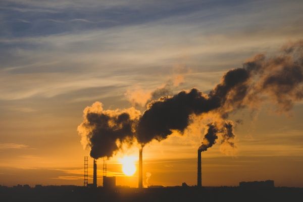 A factory with plumes of smoke coming out of several chimneys at sunset.
