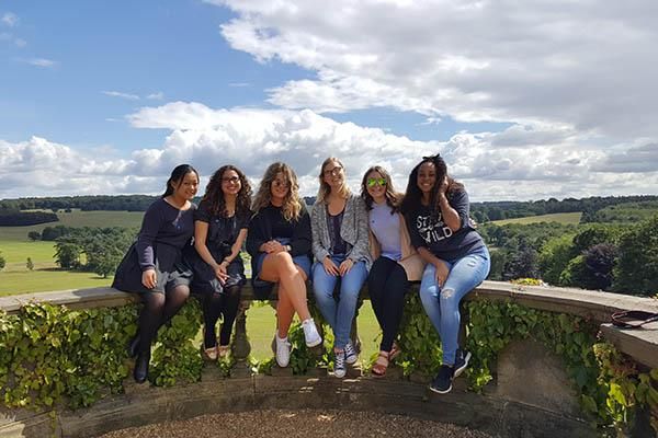 6 Leeds International Summer School students sat on a wall at Harewood House on a sunny day in 2016