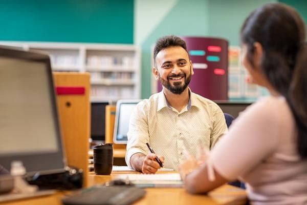 Two people sat in the Language Centre having a conversation. One is smiling and wearing a white shirt.