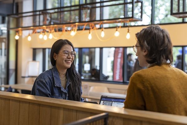 Two students sat chatting and laughing in a bright communal space on campus