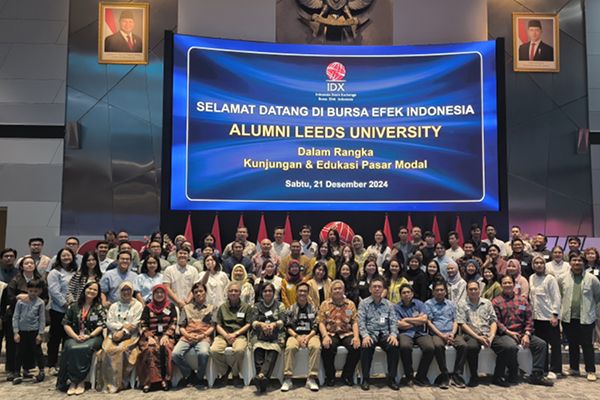 A group of alumni gather for a group photo at an event, in front of a large screen.