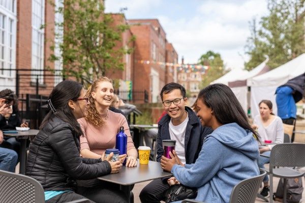 Four international students sitting at a table outside Leeds University Union building, with hot drinks.