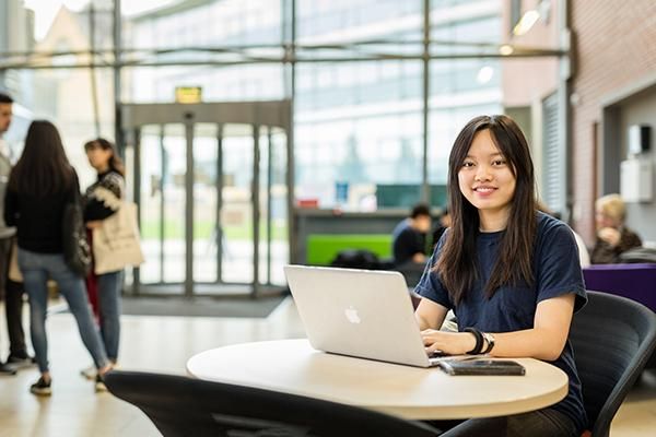 Student sat at a table with a laptop in Leeds University Business School.