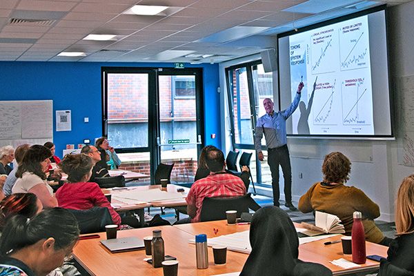 A large space with people listening to a presenter in the centre of the room.