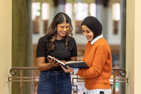 Two students looking at a book in the library and smiling.