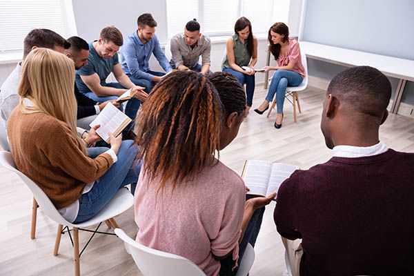 A group of ten people sat on chairs in a circle, reading from books.