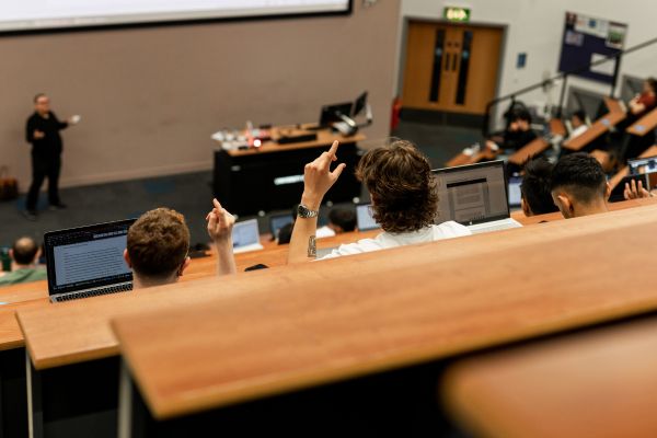 Two students in a contemporary lecture hall raising their hand to ask, or answer, a question.