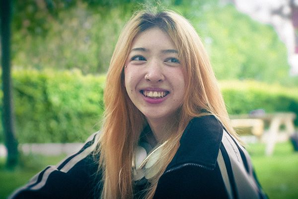 A close up of a student smiling at the camera. Lots of bright foliage is behind them.