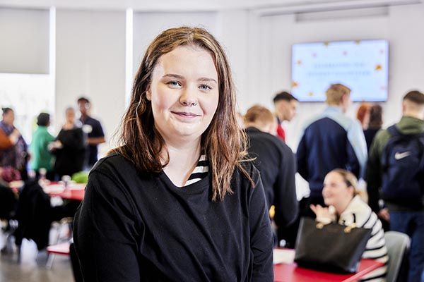 Lilly Morgan, smiling into camera in a busy classroom.