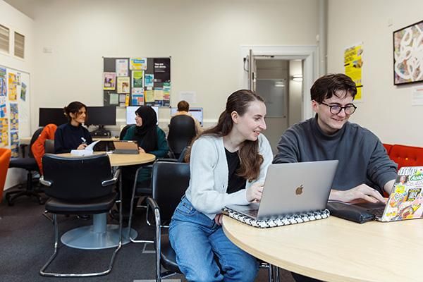 Two mature students working together at a desk with laptops