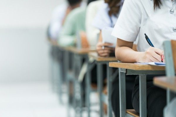 A row of anonymous schoolchildren sitting at desks writing