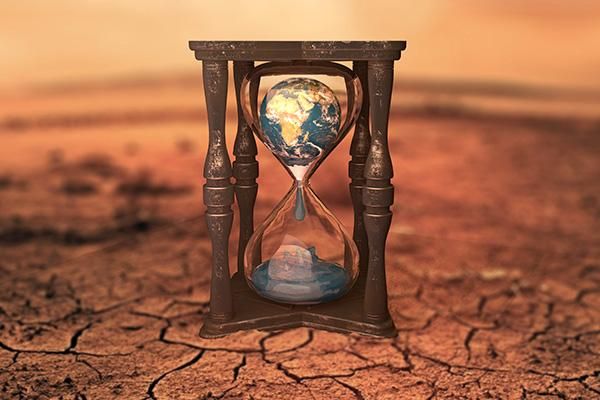 A sand timer in an arid landscape, featuring the planet Earth dripping through the sand glass.