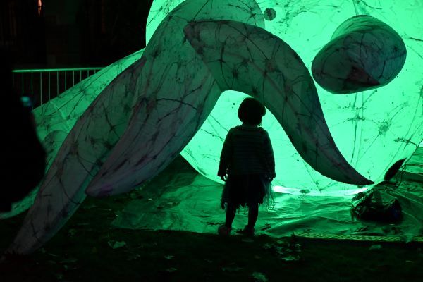 A child stands beneath a large curved shape against a glowing green background.