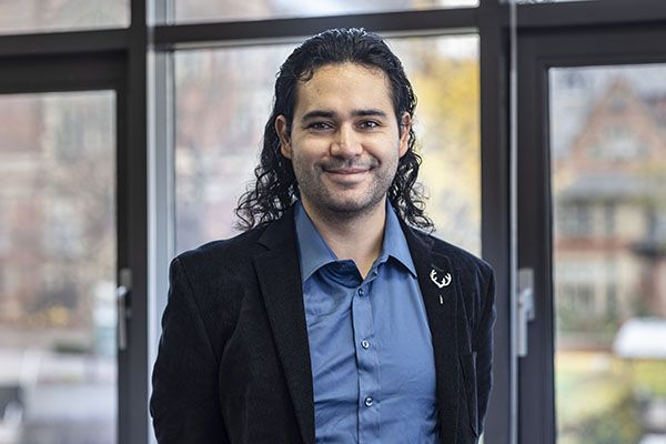 Carlos smiling in front of some windows on campus.
