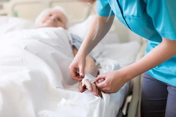 Patient in a hospital bed with a nurse fitting a cannula to their hand