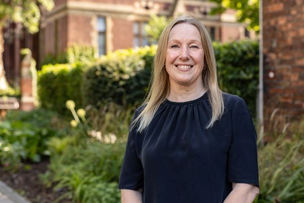 Rachel Brealey stood outside on campus on a sunny day, with trees and shrubs and red brick buildings in the background.