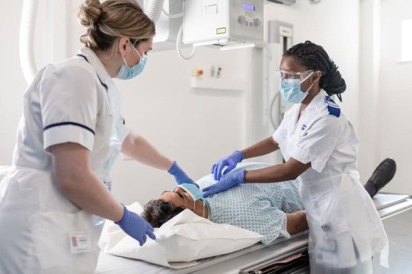 Two radiologists treating a patient, who is lying on a bed beneath a machine.