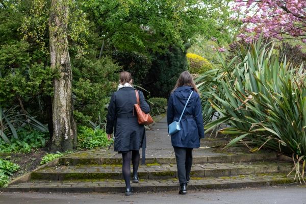 Two women walk through a park, facing away from the camera.