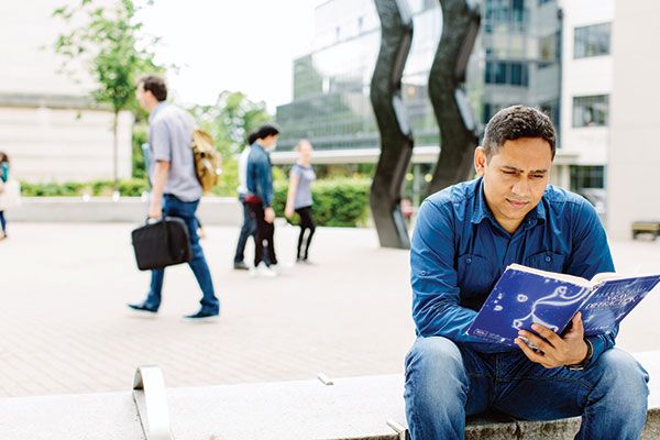 A masters student sat reading in Beech Grove Plaza near the Sign for Art sculpture.