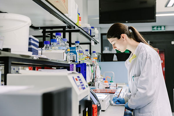 A student working in a lab writing down notes on a notepad surrounding by lab equipment