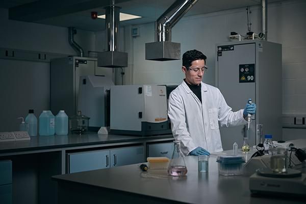 A postgraduate student in a lab wearing a white lab coat using a pipette