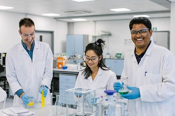 Three researchers in a lab wearing lab coats and holding test tubes and beakers