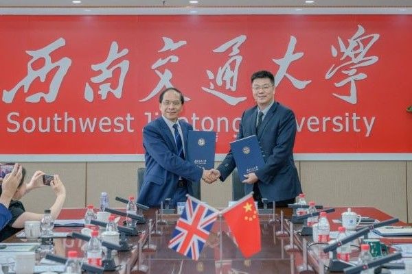 Professor Hai-Sui Yu shakes hands with Xuedong Yan in front of a sign that says 'Southwest Jiaotong University'. In front of them, the Union Jack and flag of China are crossed.