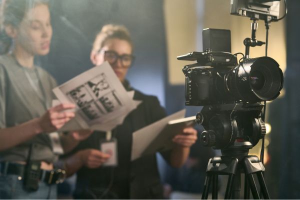 On a TV set, two workers discuss a script and storyboard behind a camera.