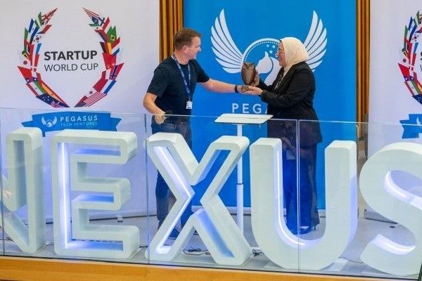 Gareth Scargill presents the winners trophy to Rania Maklad with the Nexus logo in front and Startup world cup banners in the background.